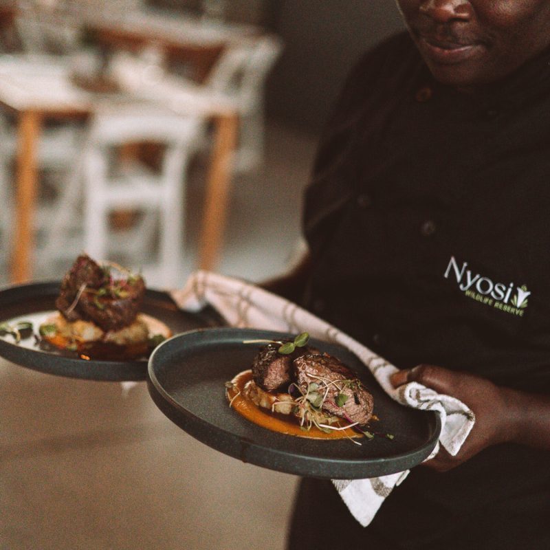 Chef at Nyosi carrying two plates of food.